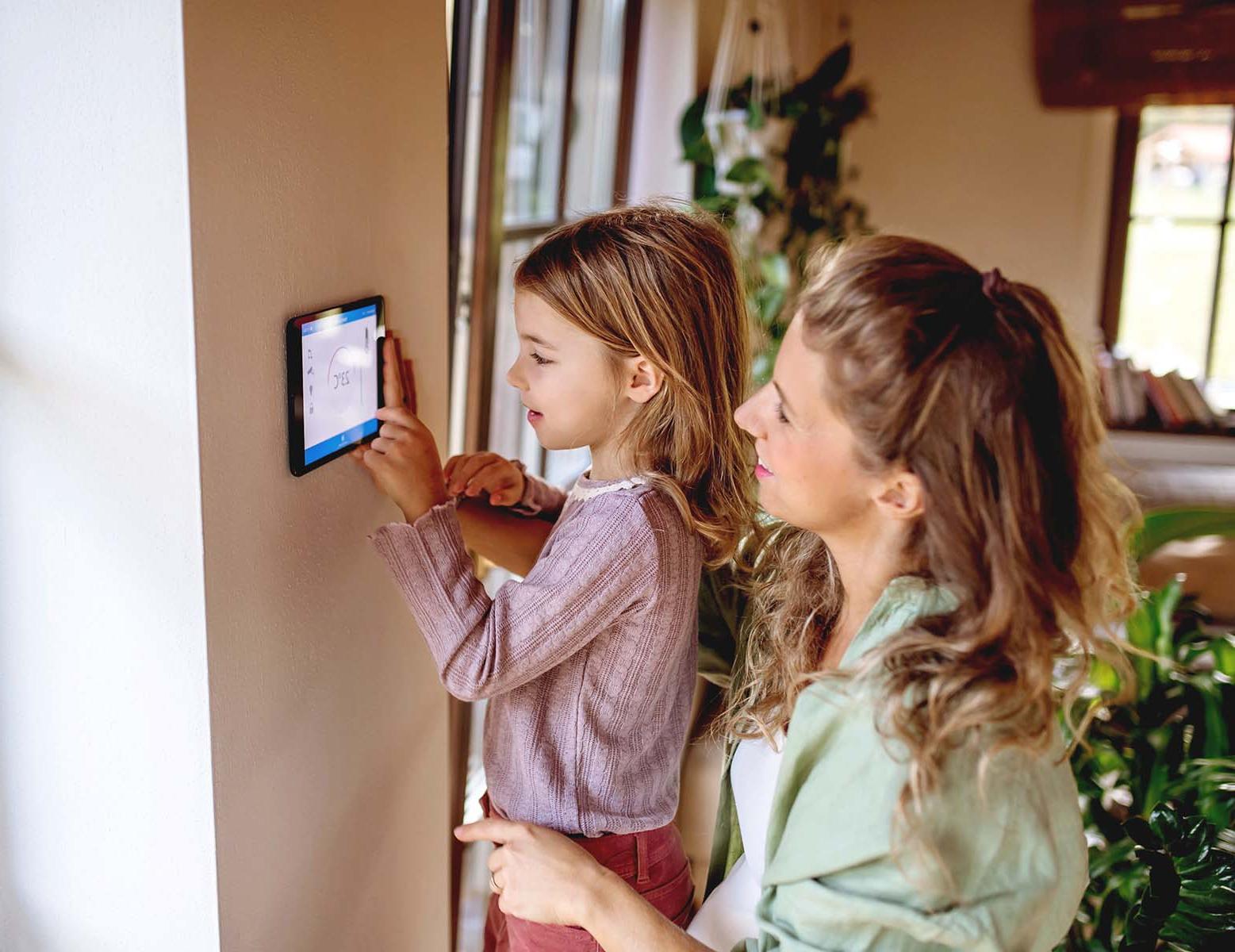 Woman and child adjusting a smart home thermostat.